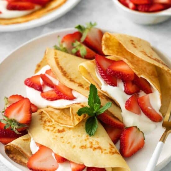 Strawberry crepes on a plate with a fork.