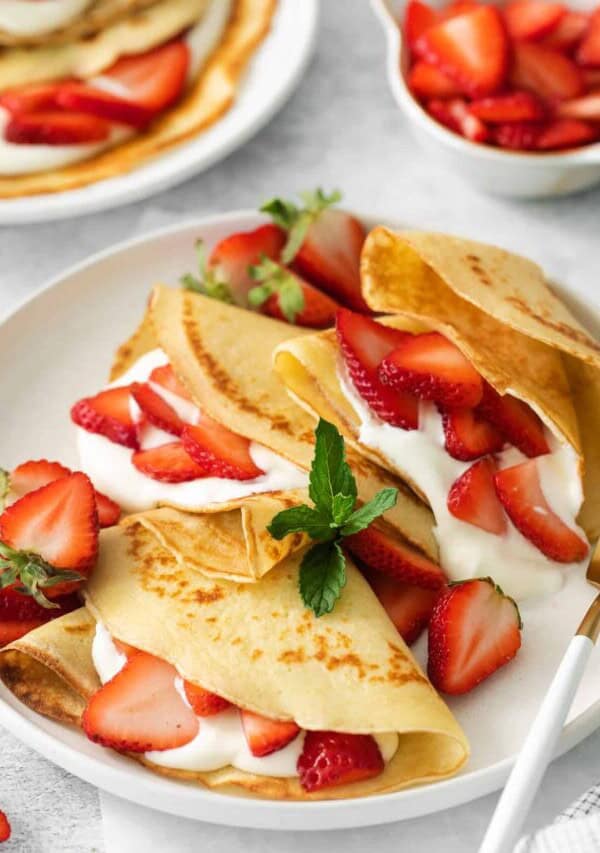 Strawberry crepes on a plate with a fork.