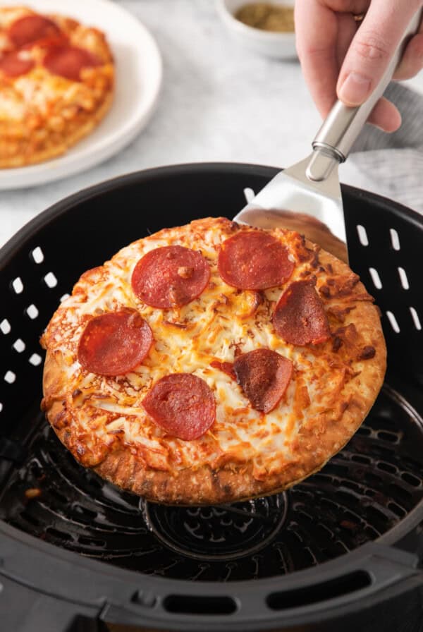 Pizza being removed from the air fryer with a spatula.