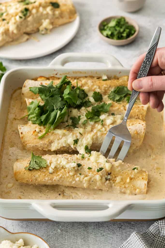 enchiladas in a white baking dish with a fork.