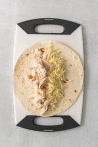 a tortilla with cheese and chicken on a cutting board.