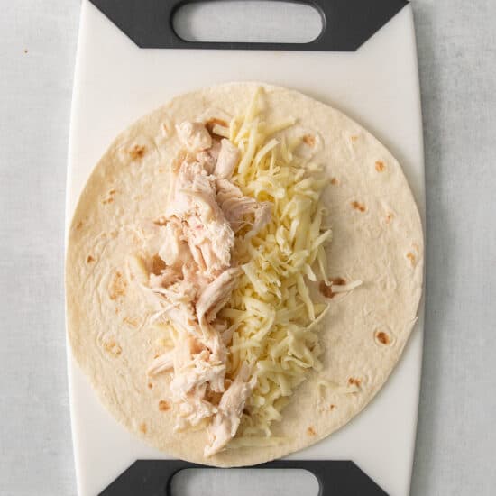 a tortilla with cheese and chicken on a cutting board.