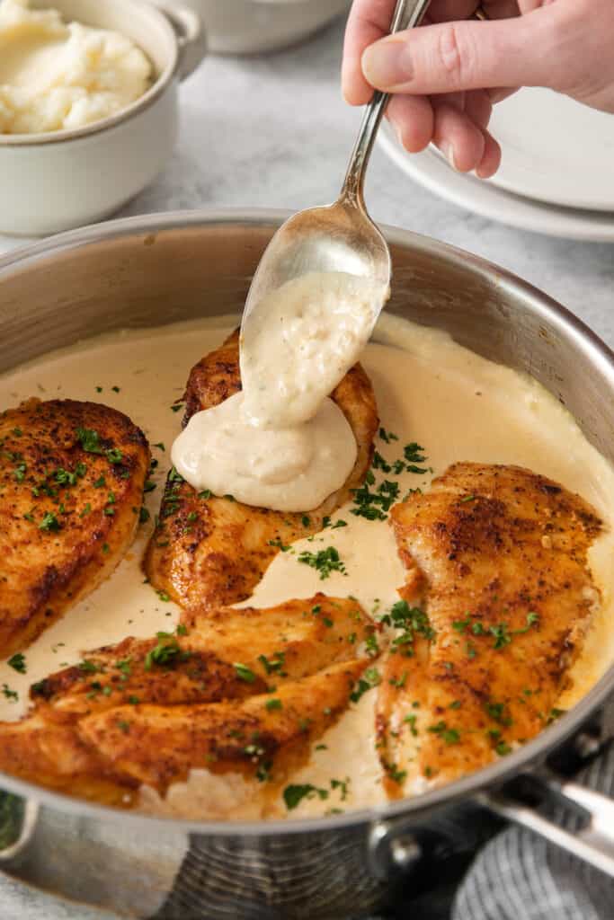 a person pouring a sauce over chicken breasts in a skillet.
