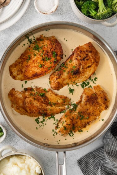 chicken breasts in a pan with mashed potatoes and broccoli.
