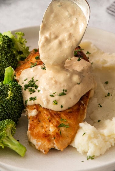 a spoon is being used to pour a sauce over chicken and broccoli on a plate.