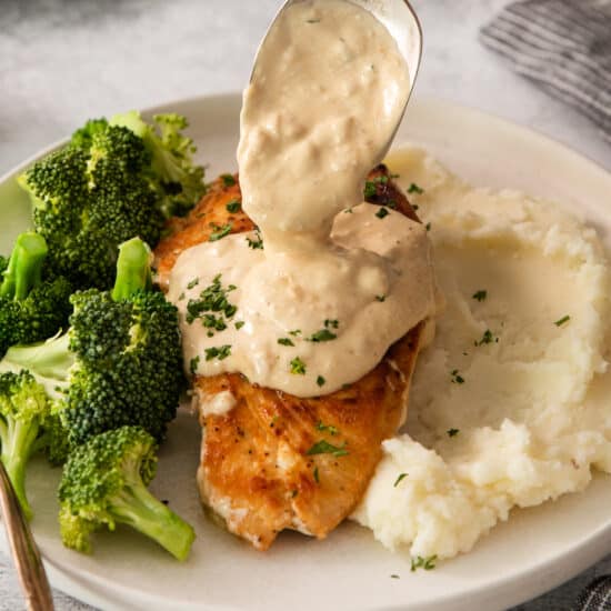 a spoon is being used to pour a sauce over chicken and broccoli on a plate.