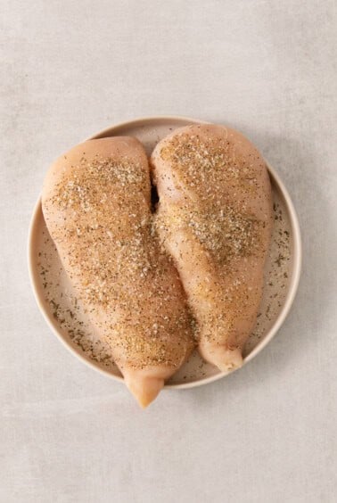 two chicken breasts on a plate with spices.
