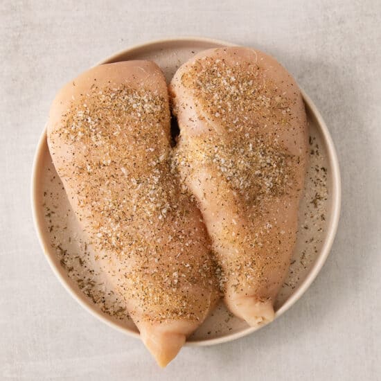 two chicken breasts on a plate with spices.
