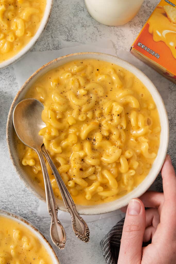 a person holding a bowl of macaroni and cheese.