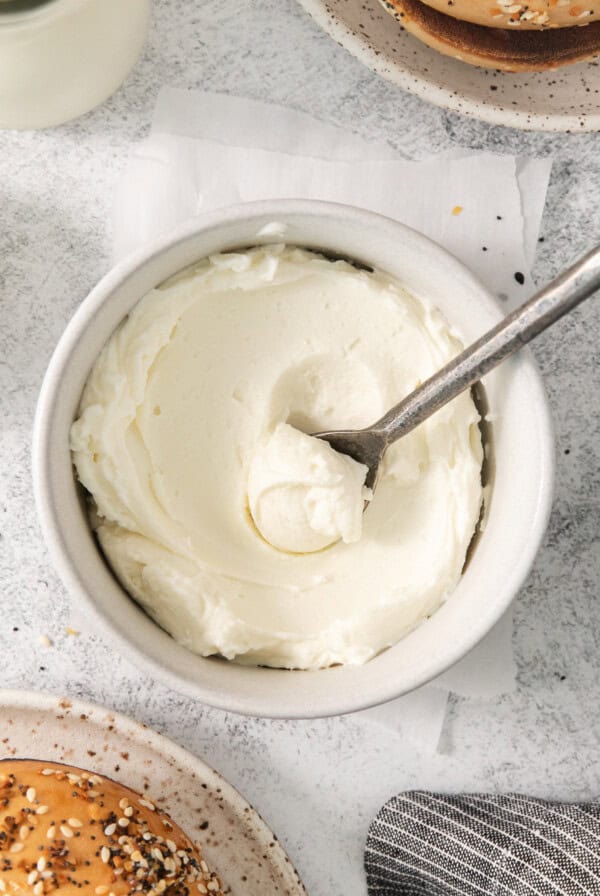 a bowl of cream cheese with a spoon next to a baguette.