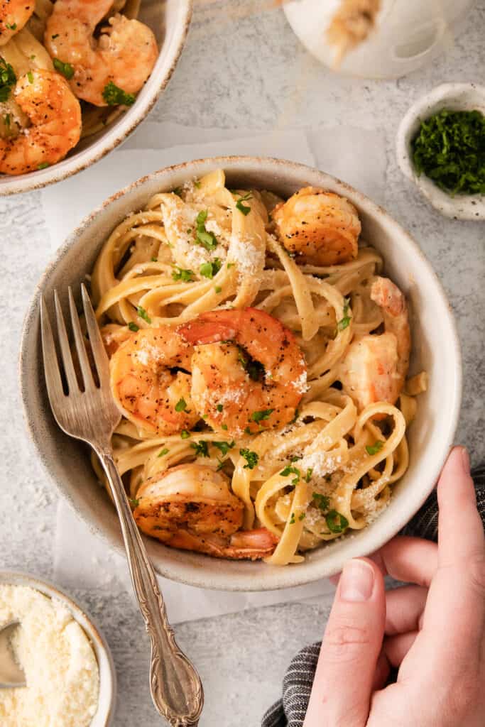 a person holding a bowl of pasta with shrimp and parmesan.