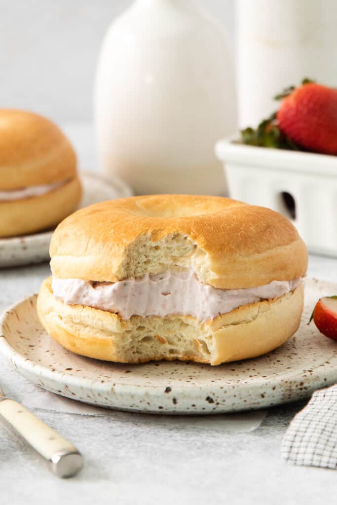 a bagel sandwich with strawberries and cream on a plate.