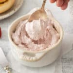 a person is scooping strawberry whipped cream into a bowl.