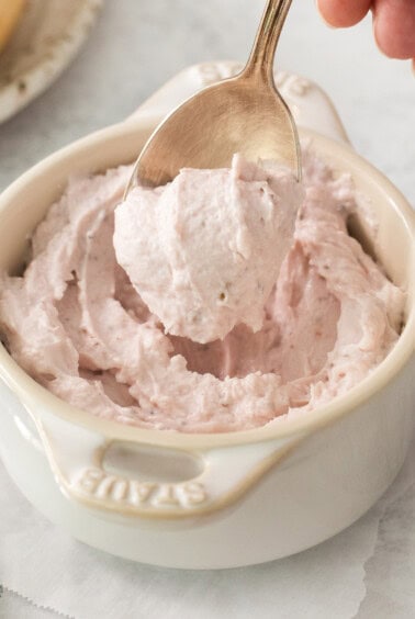 a person is scooping strawberry whipped cream into a bowl.