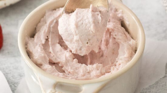 a person is scooping strawberry whipped cream into a bowl.