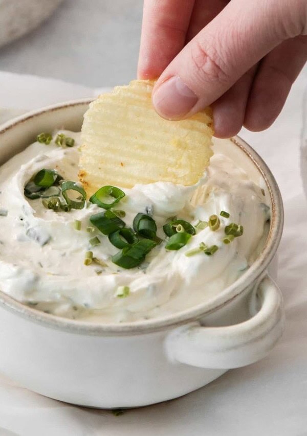 a person dipping a cracker into a bowl of dip.