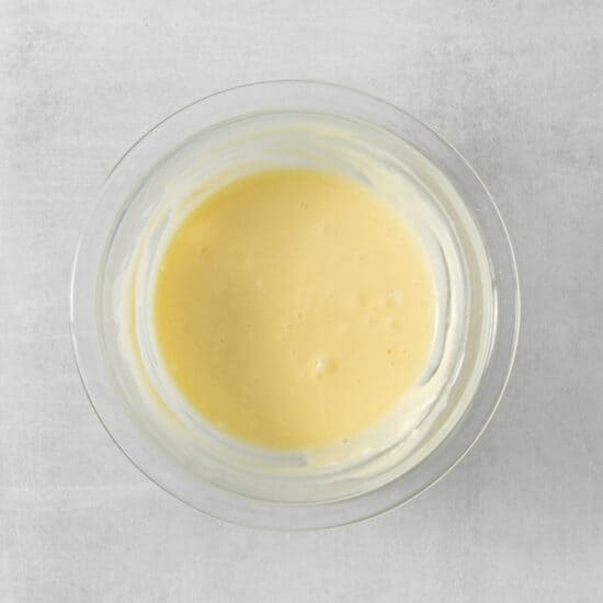 a bowl of yellow sauce on a white surface.