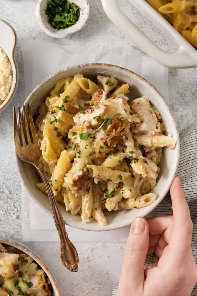 a person holding a bowl of pasta with chicken and parmesan.