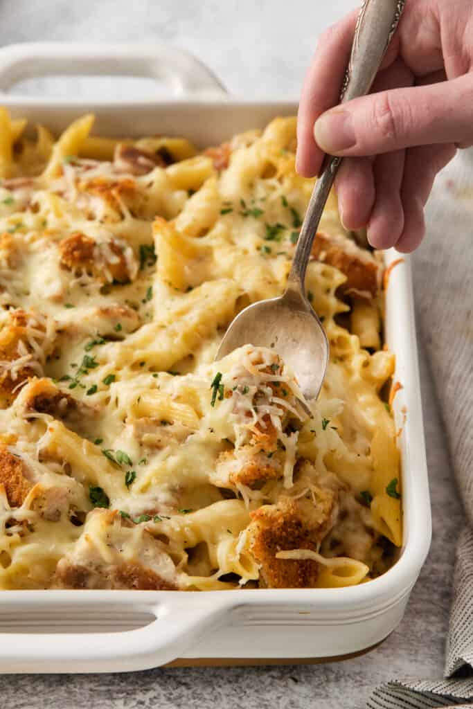 a hand reaching into a casserole dish with a spoon.