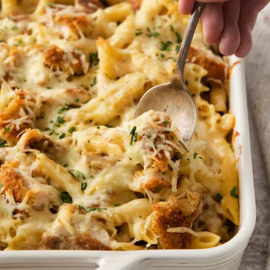 a person scooping out a casserole dish with chicken and pasta.