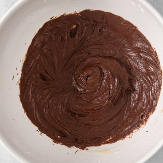 a white bowl filled with chocolate frosting on top of a table.