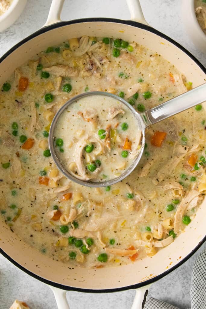 chicken chowder in a pot with peas and carrots.