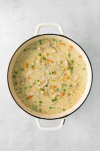 chicken chowder in a white pot with peas and carrots.