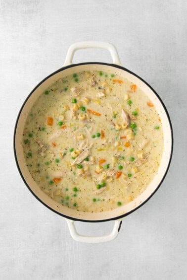 chicken chowder in a white pot with peas and carrots.