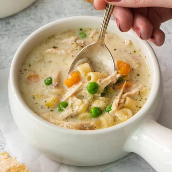 a spoonful of chicken noodle soup in a white bowl.