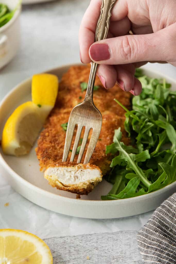 a person holding a fork on a plate with chicken and greens.