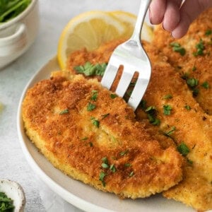 a person holding a fork to a plate of fried chicken.