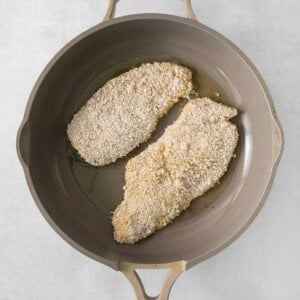 two pieces of breaded chicken in a frying pan.