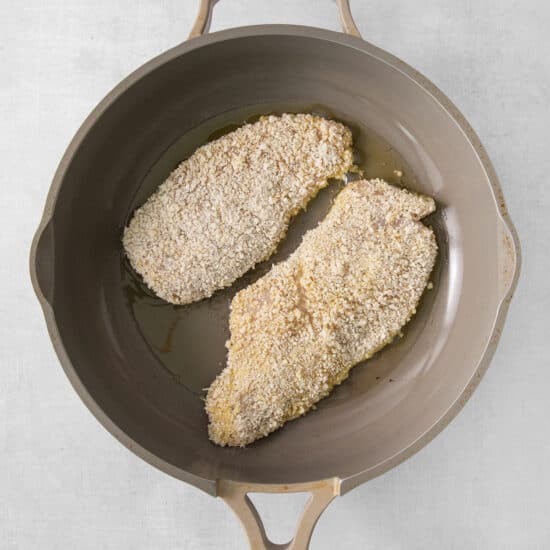 two pieces of breaded chicken in a frying pan.