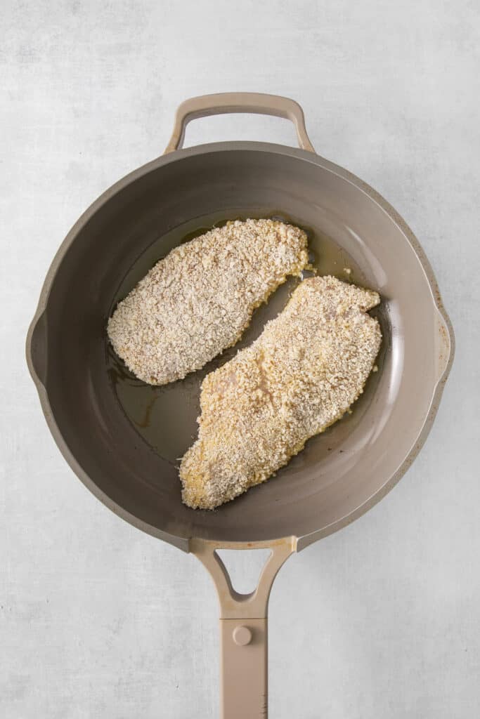 two pieces of breaded chicken in a frying pan.