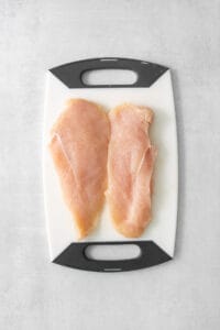 two chicken breasts on a cutting board.