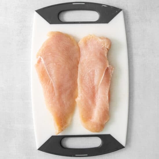 two chicken breasts on a cutting board.