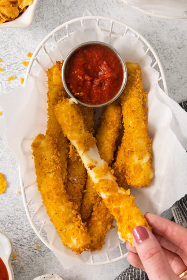 a person holding a basket of fried fish sticks with dipping sauce.