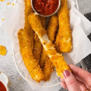 a person holding a basket of fried chicken sticks with dipping sauce.