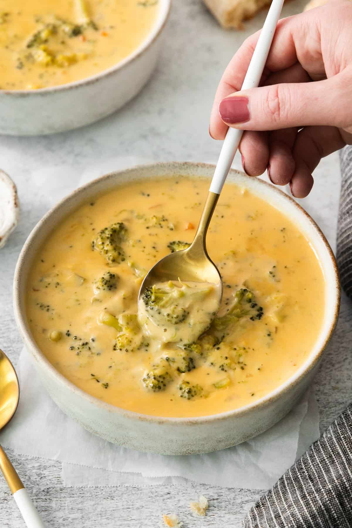 a person holding a spoonful of broccoli soup in a bowl.