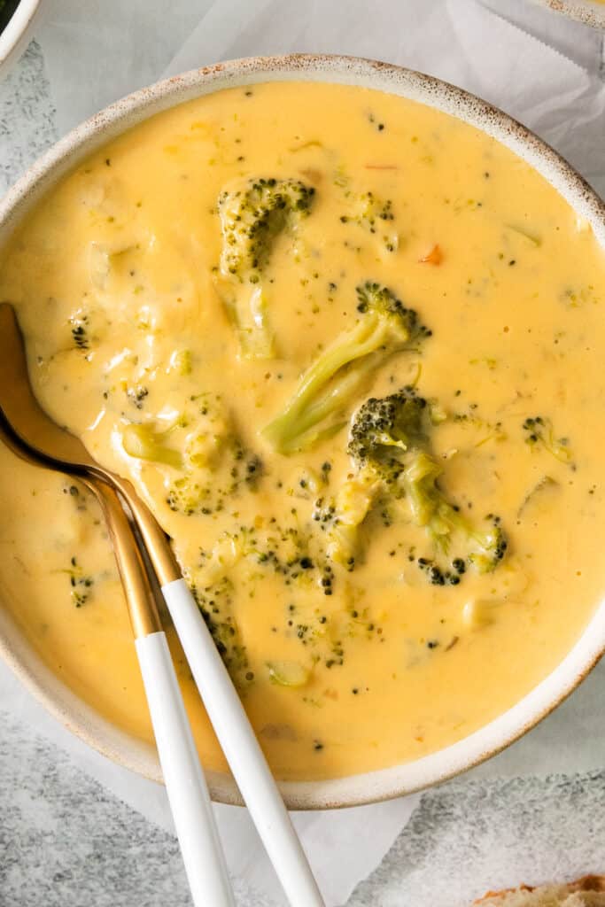 a bowl of broccoli cheese soup with two spoons.