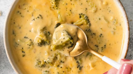 a bowl of broccoli cheese soup with a hand holding a spoon.