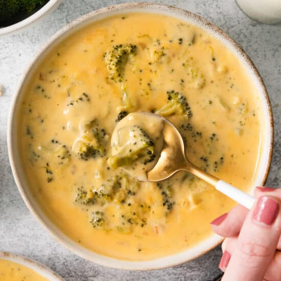 a bowl of broccoli cheese soup with a hand holding a spoon.