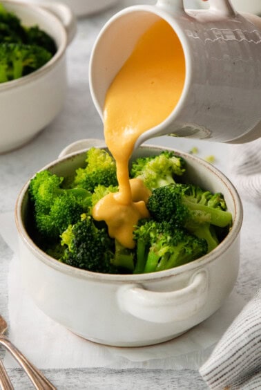 a person pouring sauce onto a bowl of broccoli.