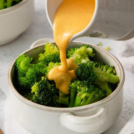 a person pouring sauce onto a bowl of broccoli.