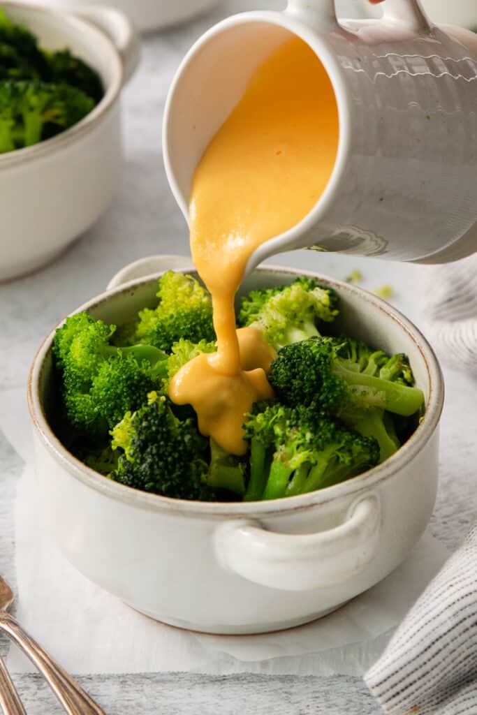 a person pouring sauce onto a bowl of broccoli.