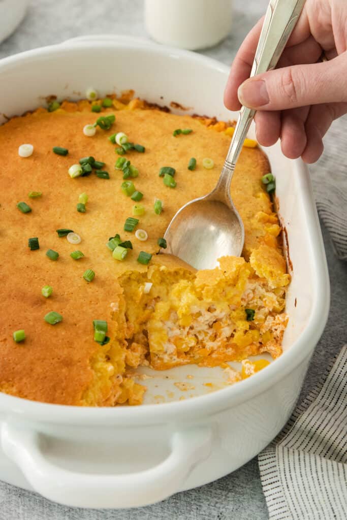 a person holding a spoon in a casserole dish.