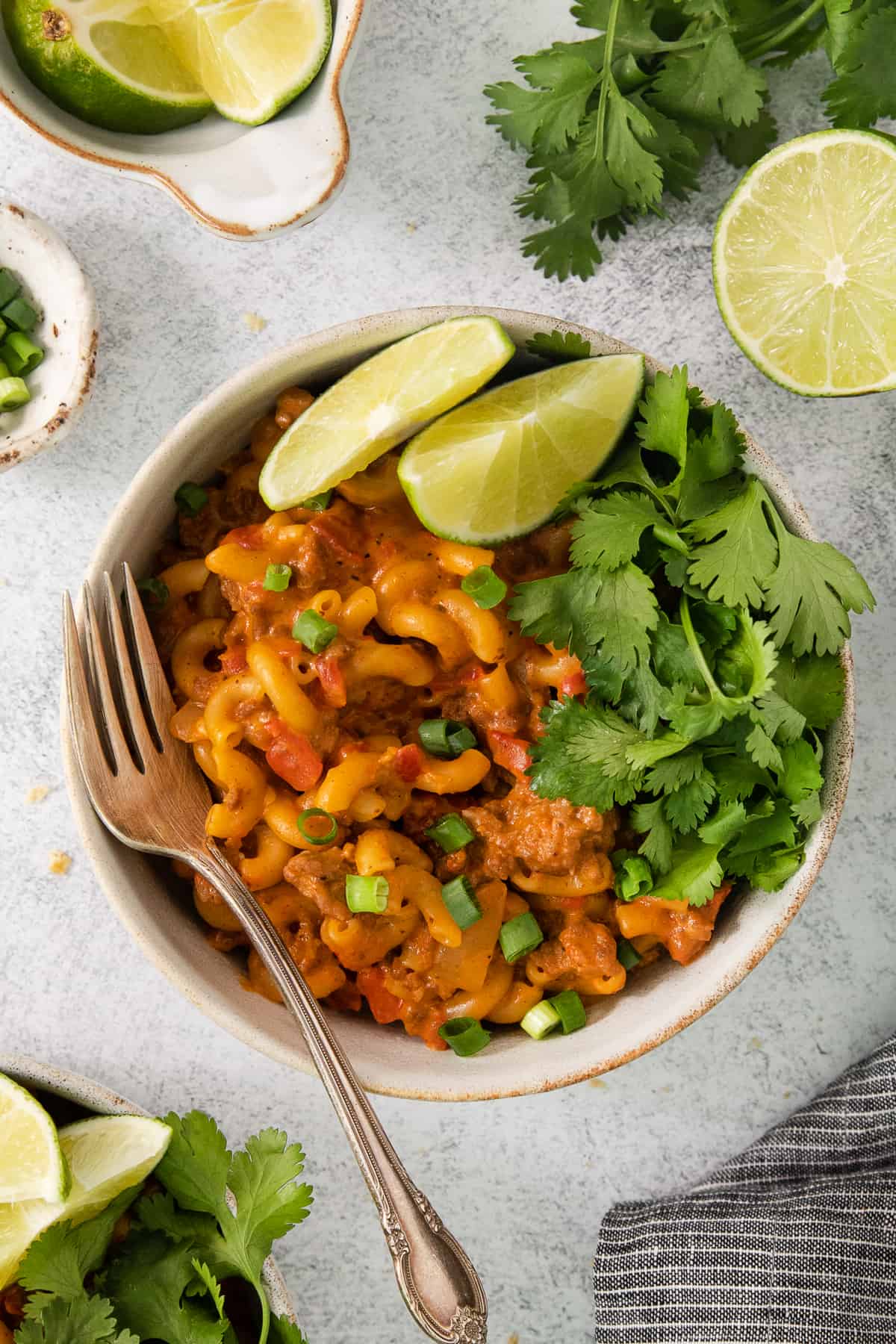 a bowl of mexican macaroni and cheese with lime wedges.