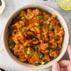 a person holding a bowl of mexican macaroni and cheese.