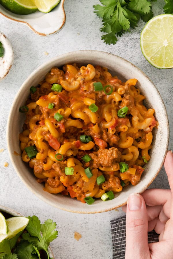 a person holding a bowl of mexican macaroni and cheese.