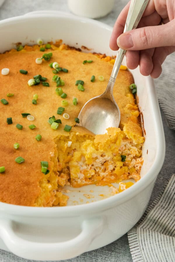 a person holding a spoon in a casserole dish.